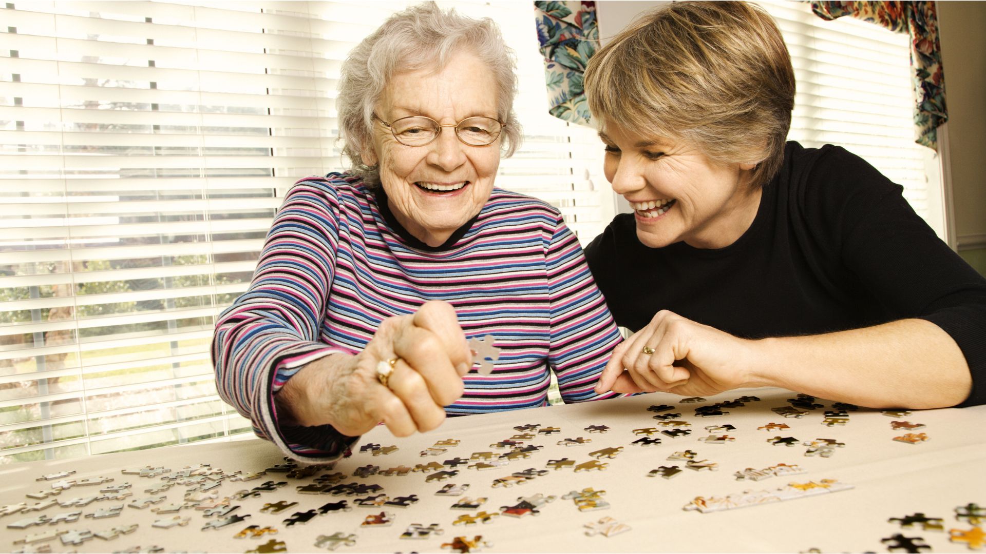 Elderly woman playing jigsaw puzzle game with her daughter, symbolizing national forget-me-not day