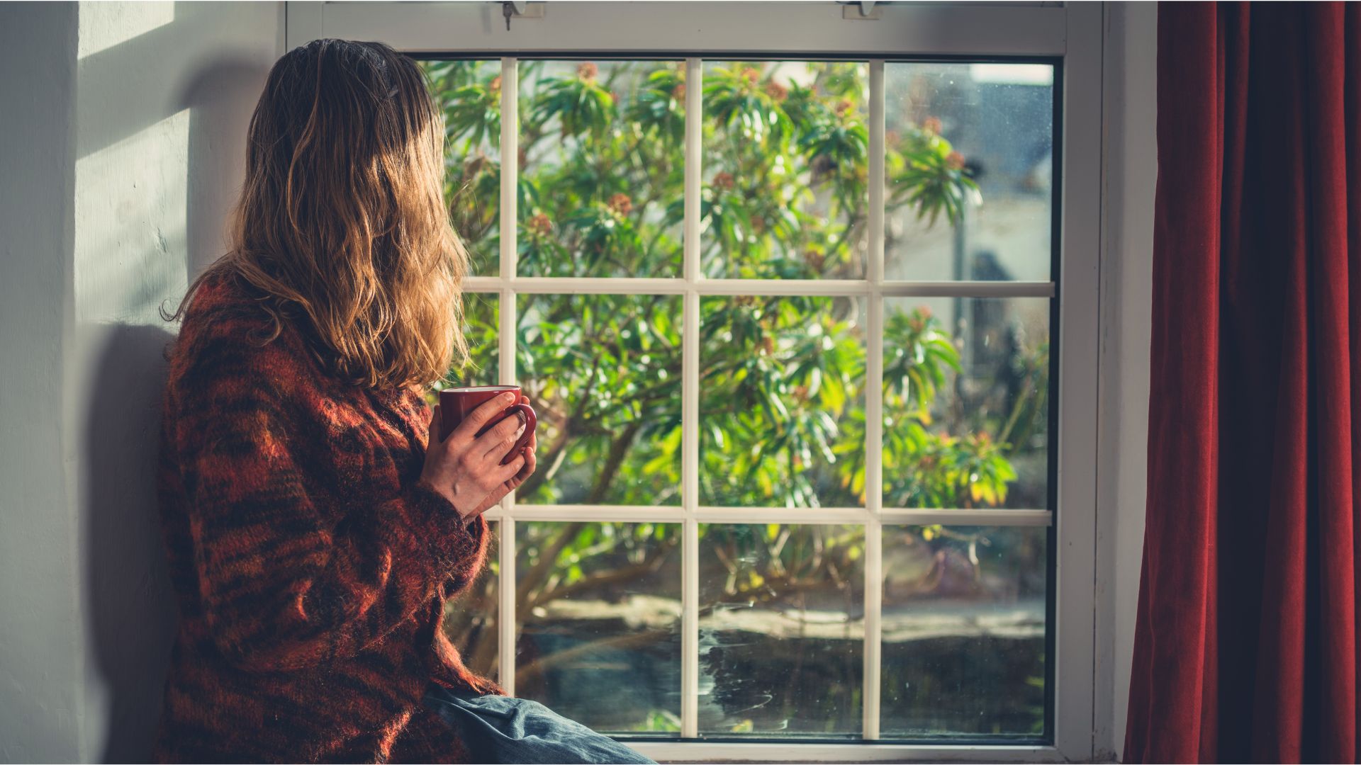 A person sitting peacefully by a window and relaxing, symbolizing calm and mental clarity through stress management.