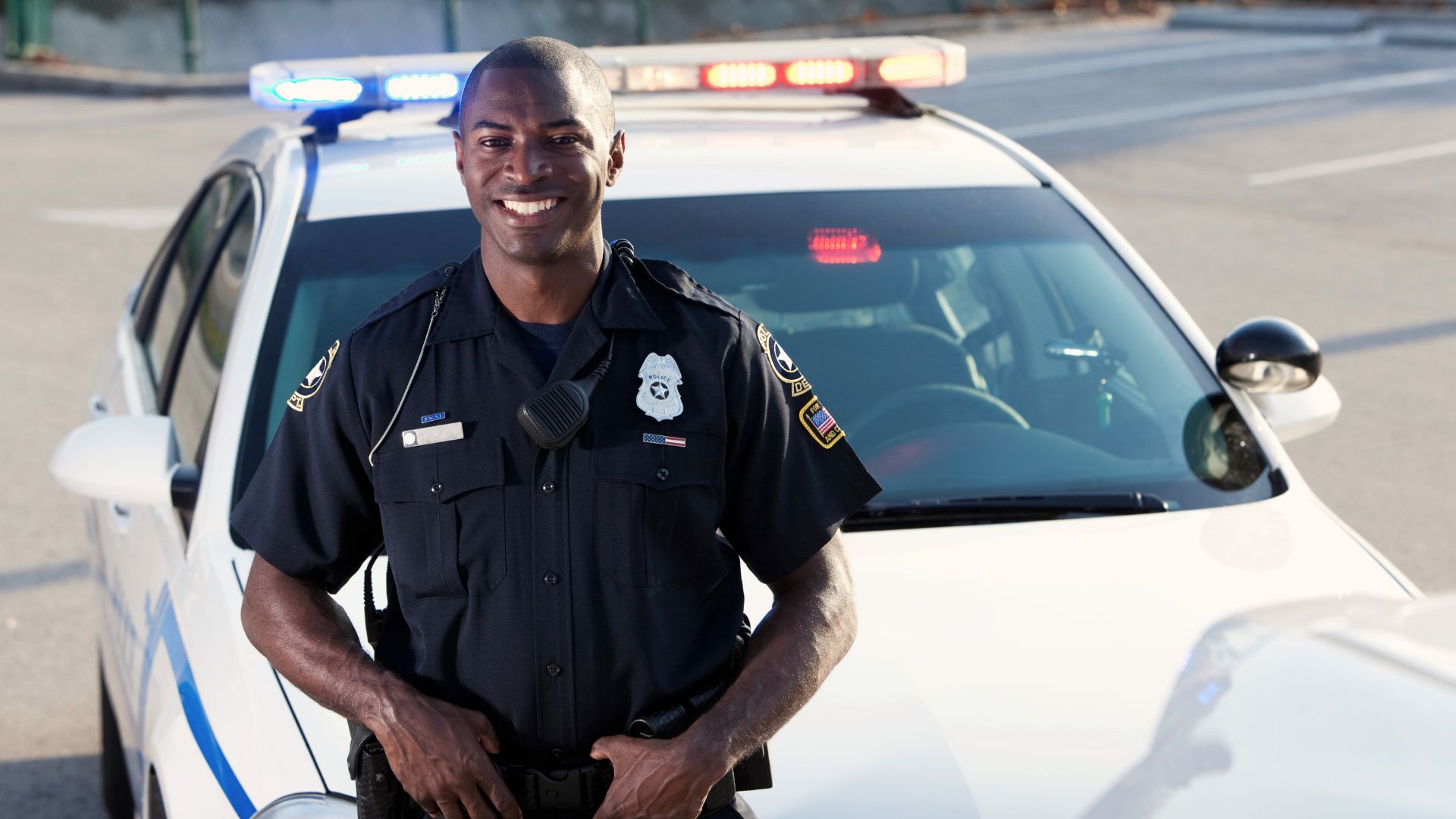 A law enforcement officer standing next to a patrol car, representing service, sacrifice, and public trust.